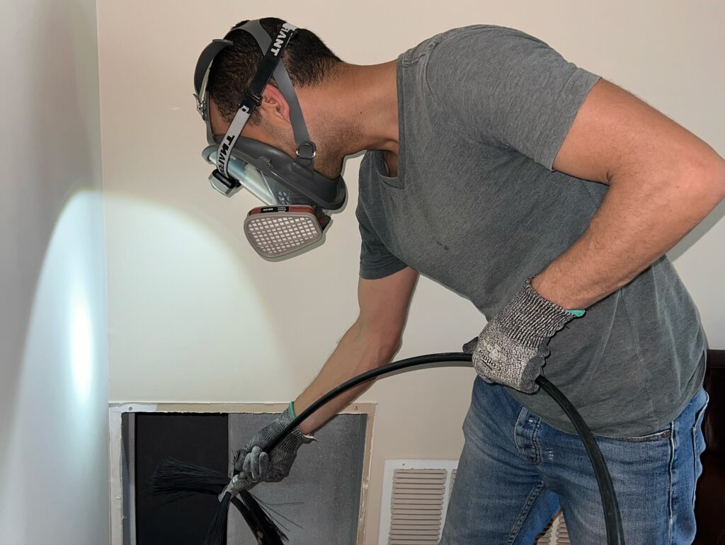 Worker wearing a respirator and gloves while cleaning a vent.